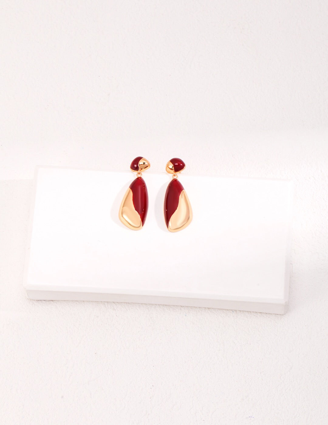 A pair of minimalist drip glaze earrings in red and gold, handcrafted in 18ct gold vermeil and sterling silver, displayed on a white block against a soft neutral background.