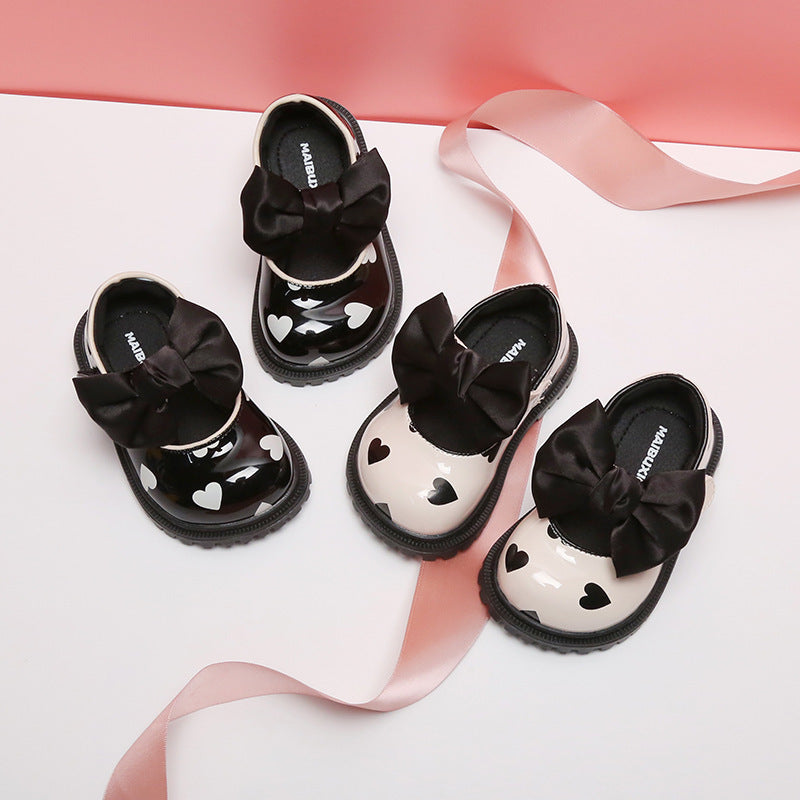 "Glossy toddler shoes with heart details and large black bows, ideal for everyday play with a princess look."