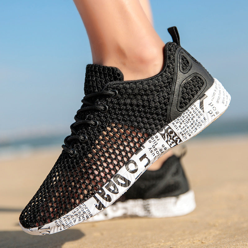 Side view of black men’s breathable mesh sneakers on a sunny boardwalk, featuring a printed rubber sole and lace-up closure.