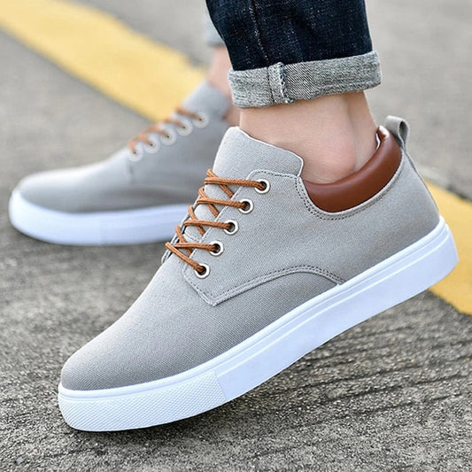 Men's breathable canvas sport shoes in grey with white sole and brown trim, displayed on street surface.