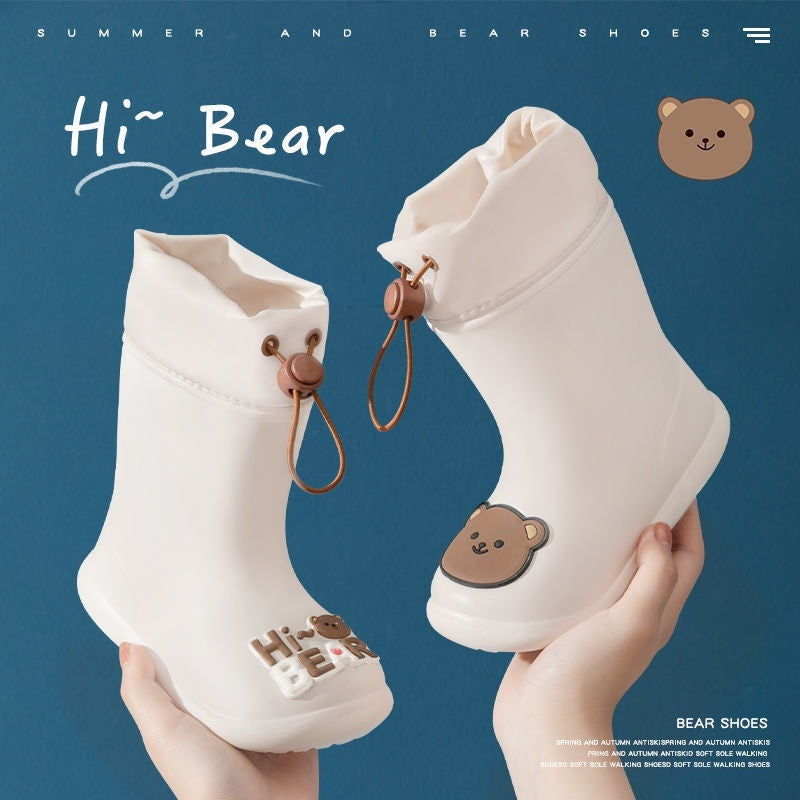 “White baby rain boots with teddy bear face, ‘Hi Bear’ lettering and drawstring elastic top – waterproof and non-slip PVC sole with a blue background”

