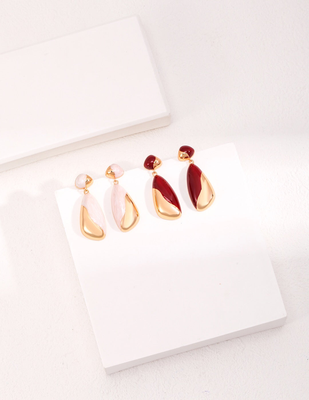 "A set of minimalist drip glaze earrings in soft pink, white, and deep red tones with 18ct gold vermeil teardrop accents, arranged on a clean white display.