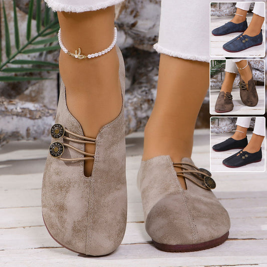 "Beige suede flat shoes for women with button detail, worn with white jeans and pearl anklet, on wooden floor"