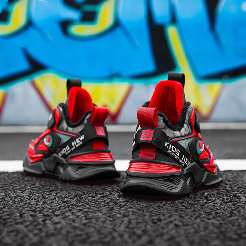 Bold red and black boys’ sneakers with thick sole and soft velvet lining, placed on textured asphalt background.