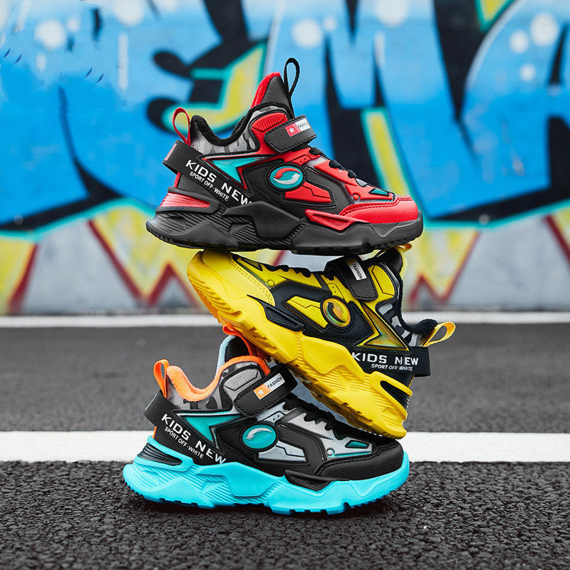 Stacked boys' sneakers in red, yellow, and aqua blue with bold design and chunky soles, photographed on asphalt in front of a colorful urban wall.

