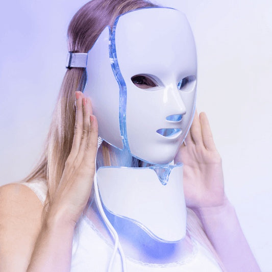 A white LED facial mask with multiple light settings, displayed on a clean surface with plug adapters beside it – designed for anti-acne and skincare therapy at home.